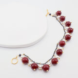 Bracelet with burgundy and white beads on dark chain with gold accents on a white background
