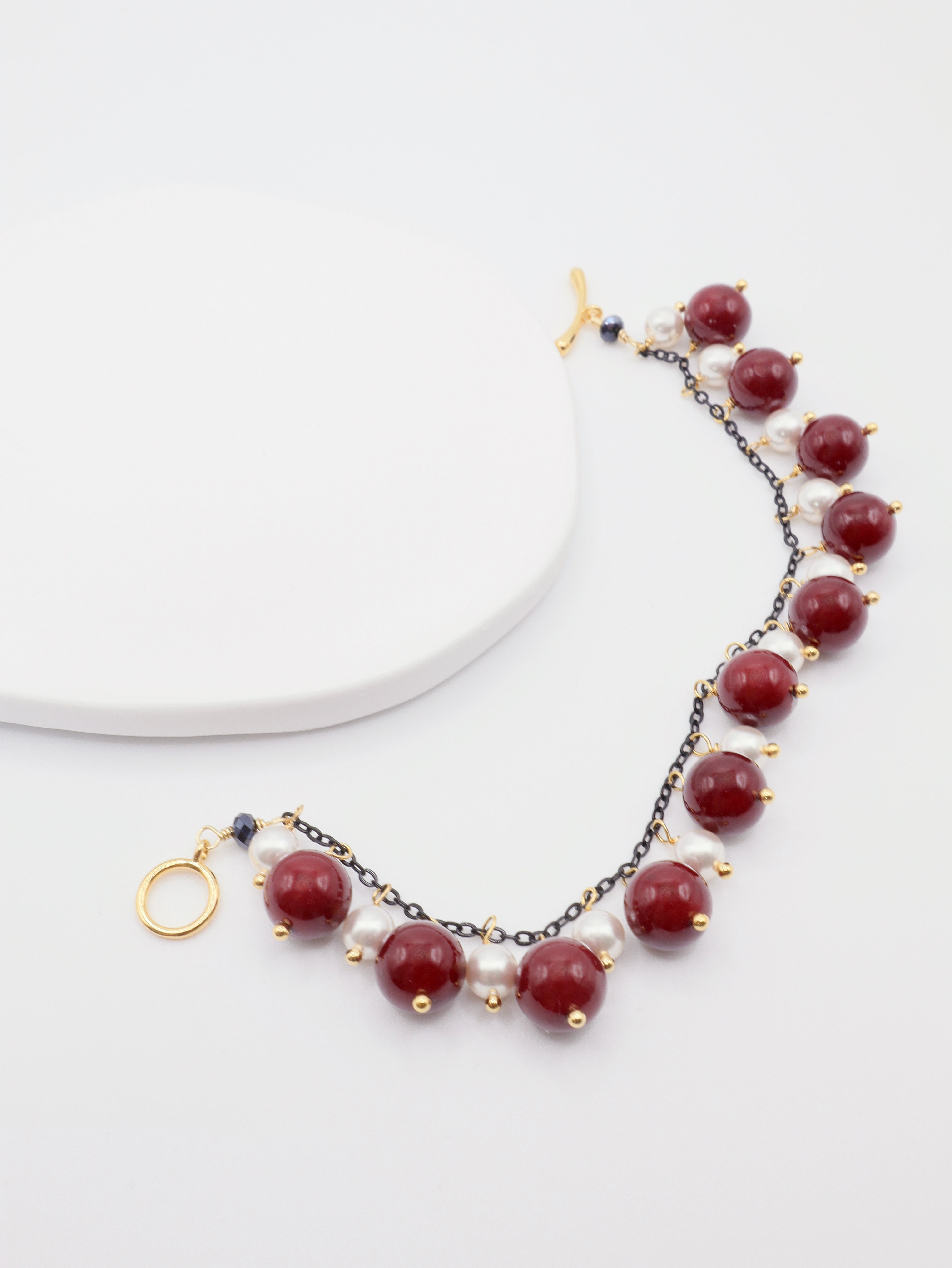 Bracelet with burgundy and white beads on dark chain with gold accents on a white background