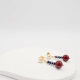 Pair of earrings with burgundy shell pearls and jet beads on a white surface