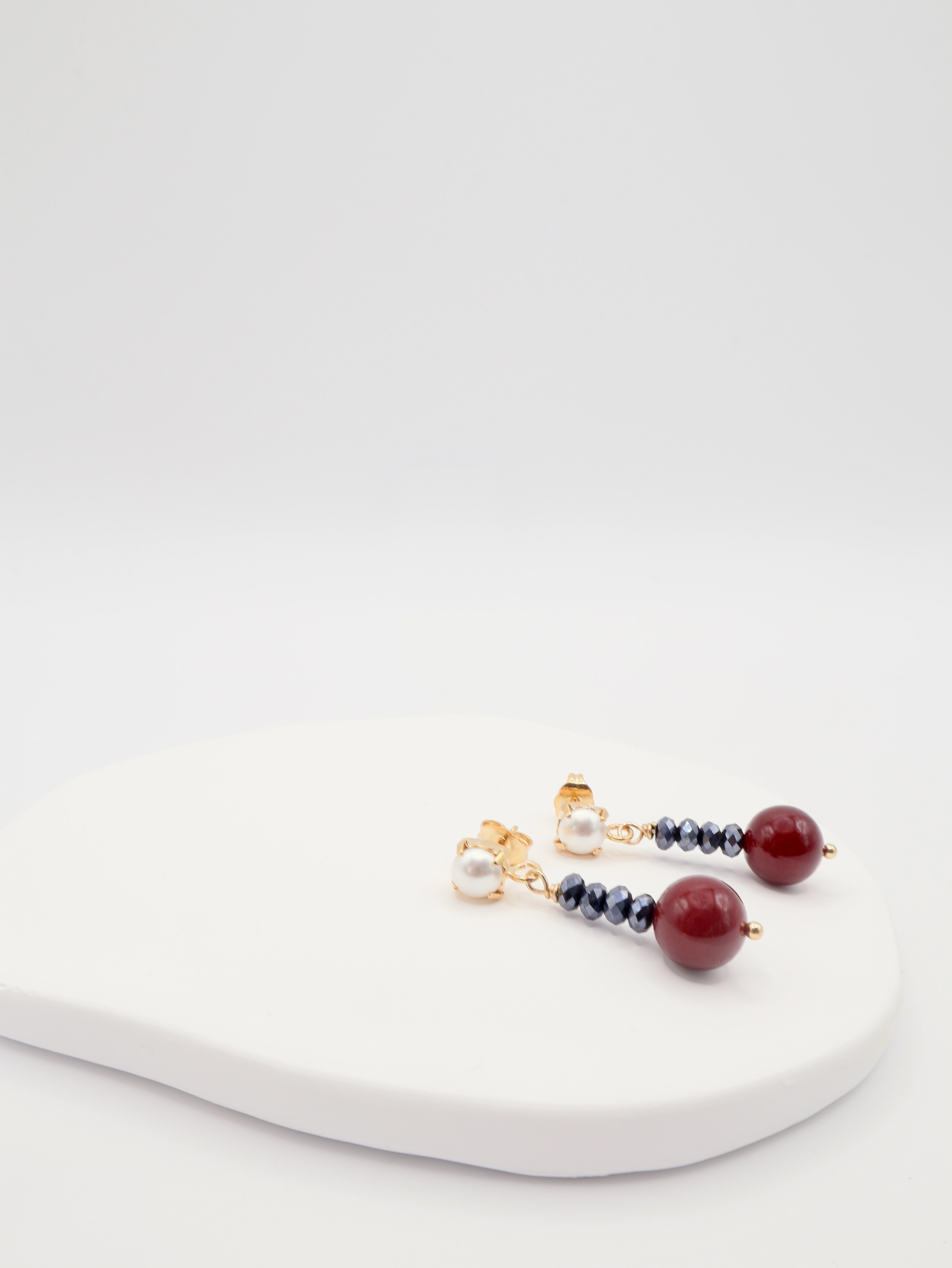 Pair of earrings with burgundy shell pearls and jet beads on a white surface
