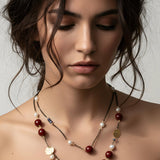 Woman wearing a layered necklace with pearls and red beads on a neutral background