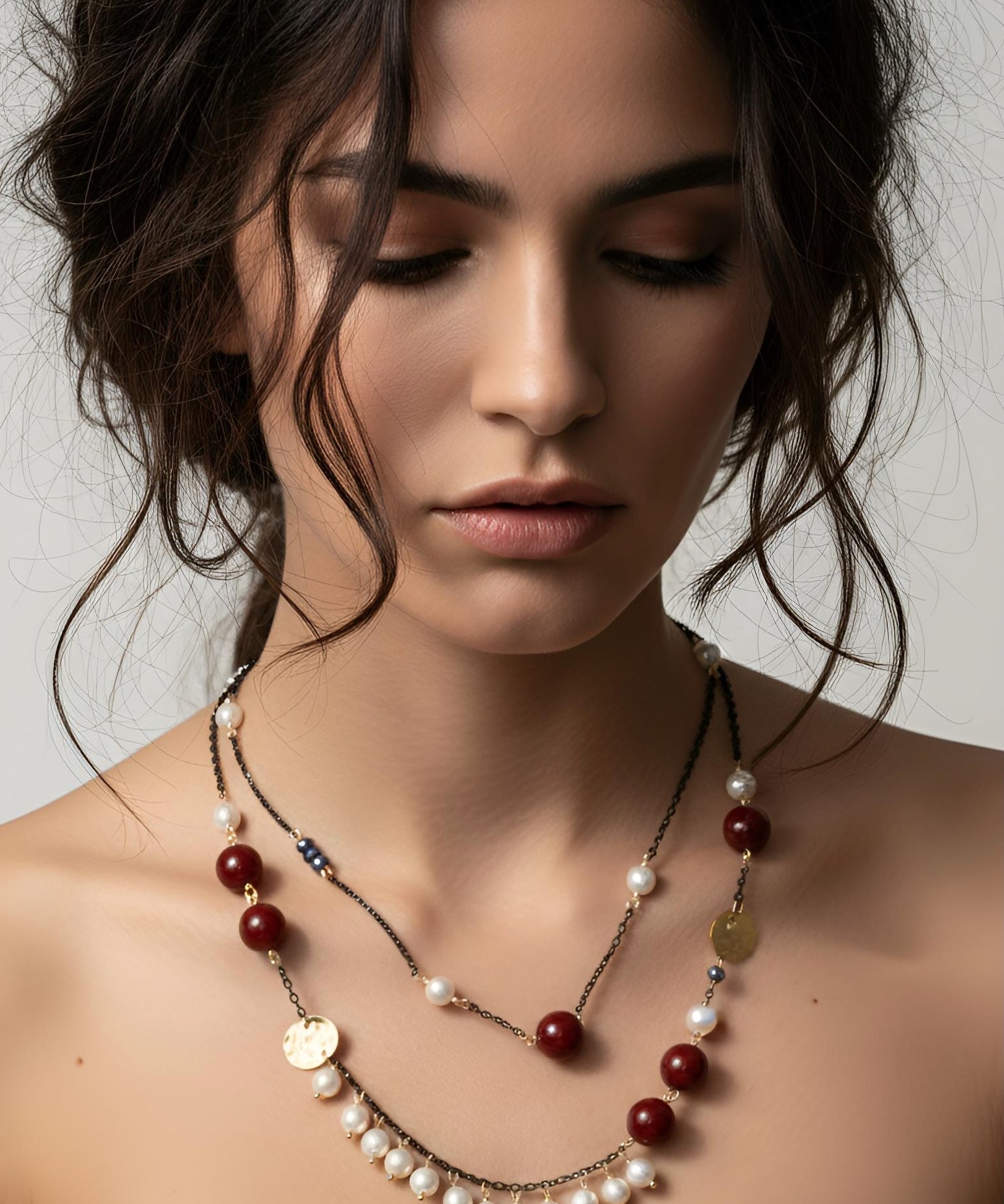 Woman wearing a layered necklace with pearls and red beads on a neutral background