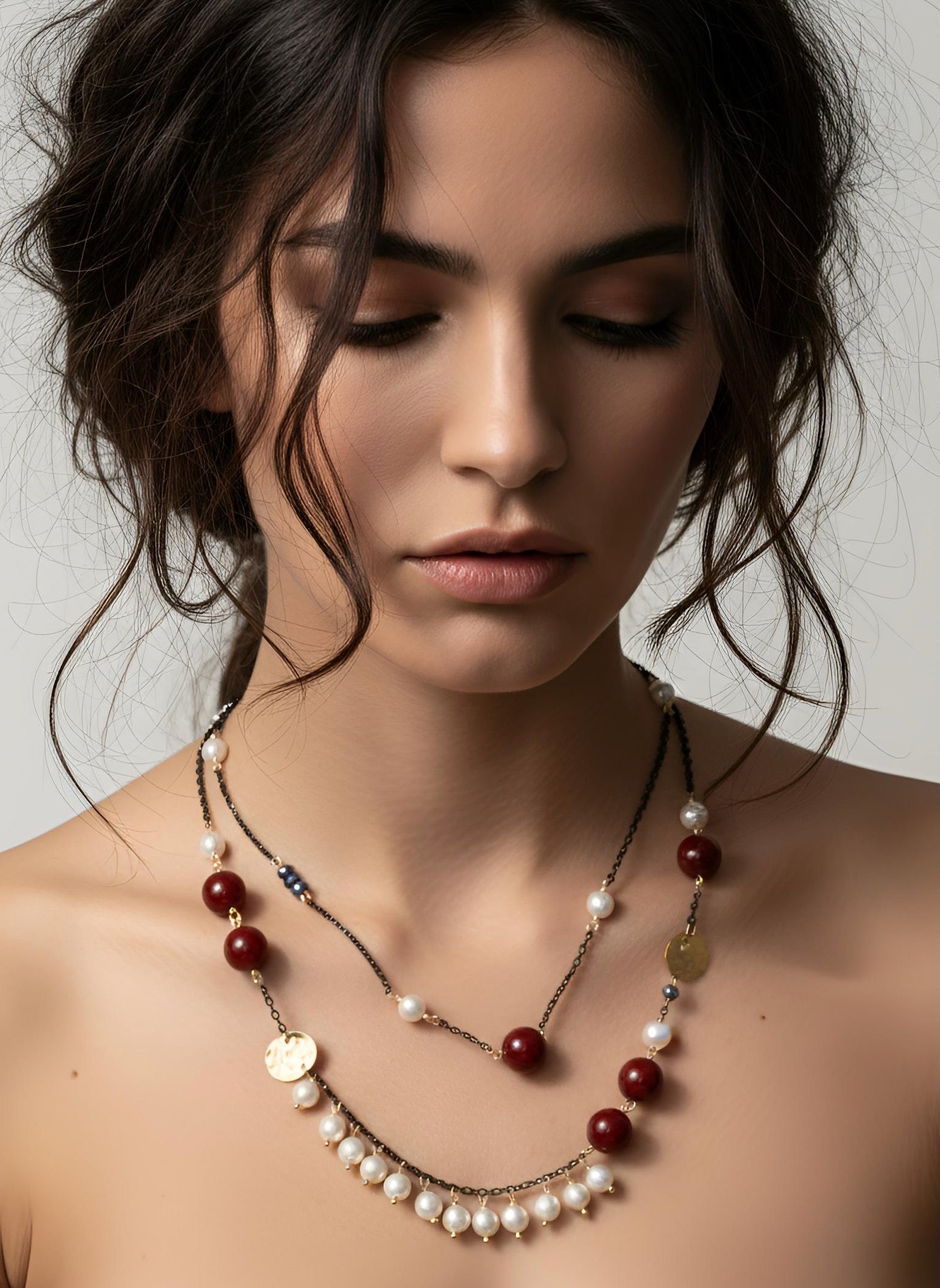 Woman wearing a layered necklace with pearls and red beads on a neutral background