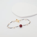 Delicate bracelet with burgundy shell and gold clasp on a white background
