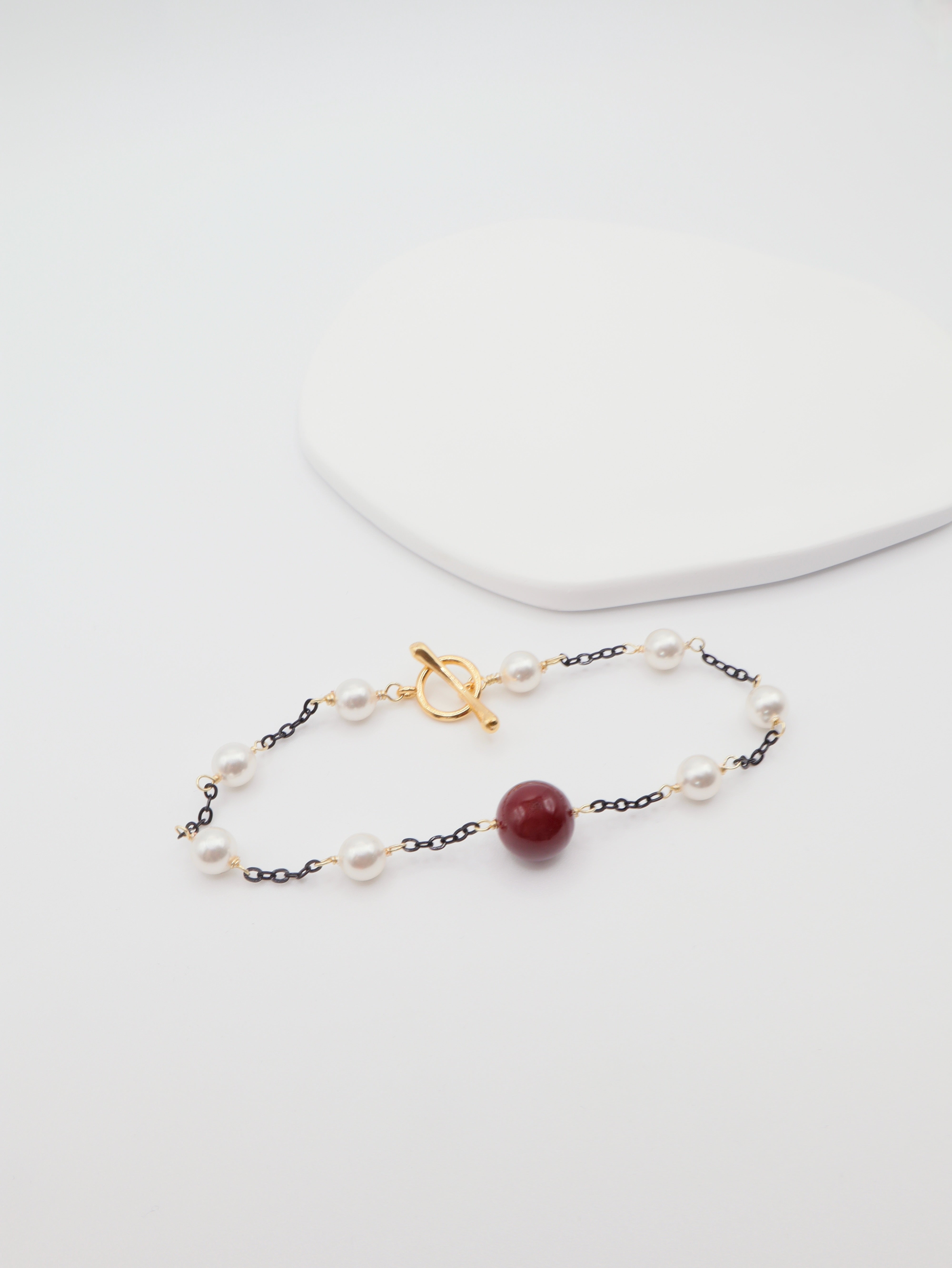 Delicate bracelet with burgundy shell and gold clasp on a white background