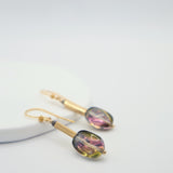 Gold earrings with coloruful glass stones on a light grey background