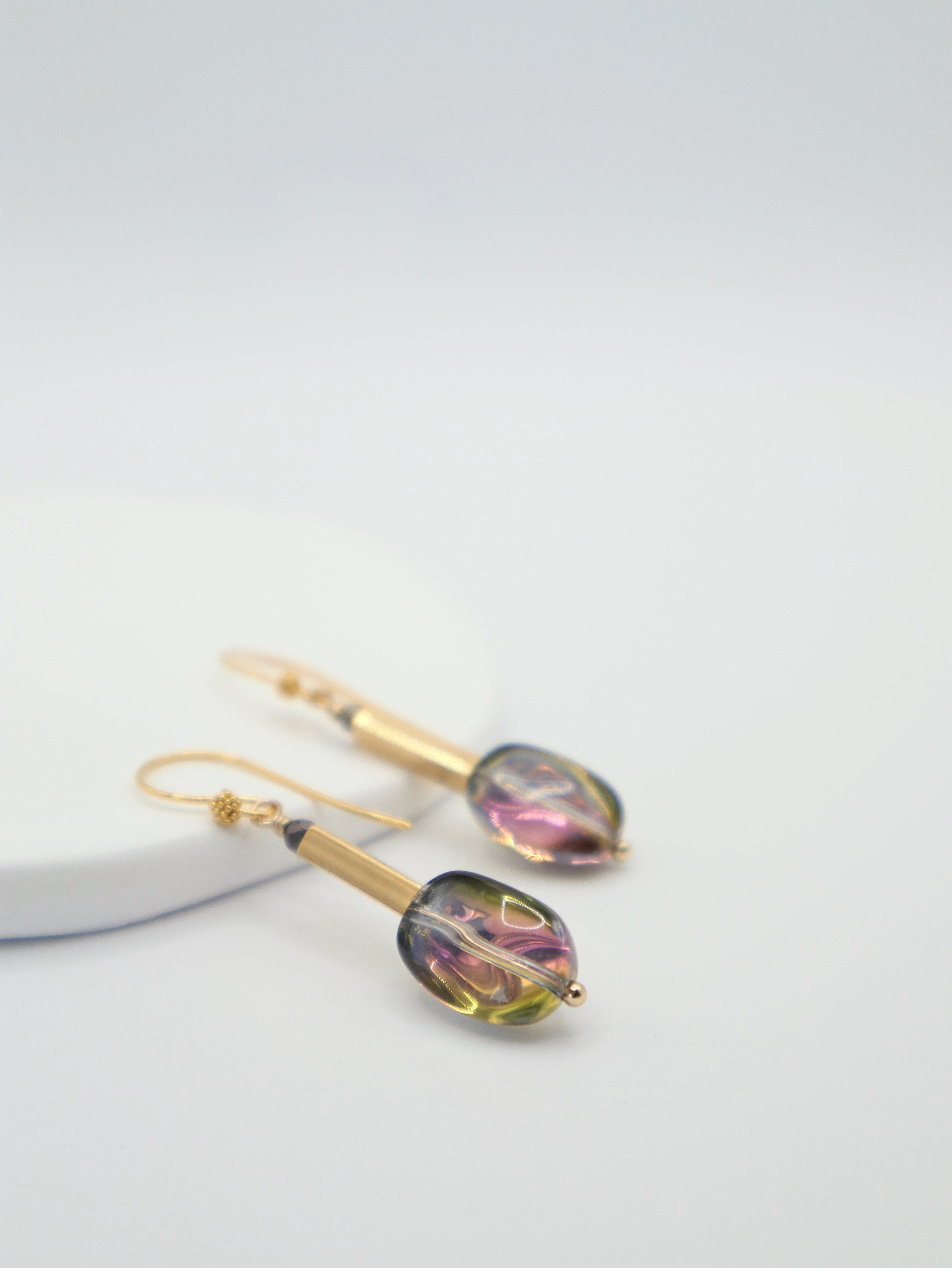 Gold earrings with coloruful glass stones on a light grey background