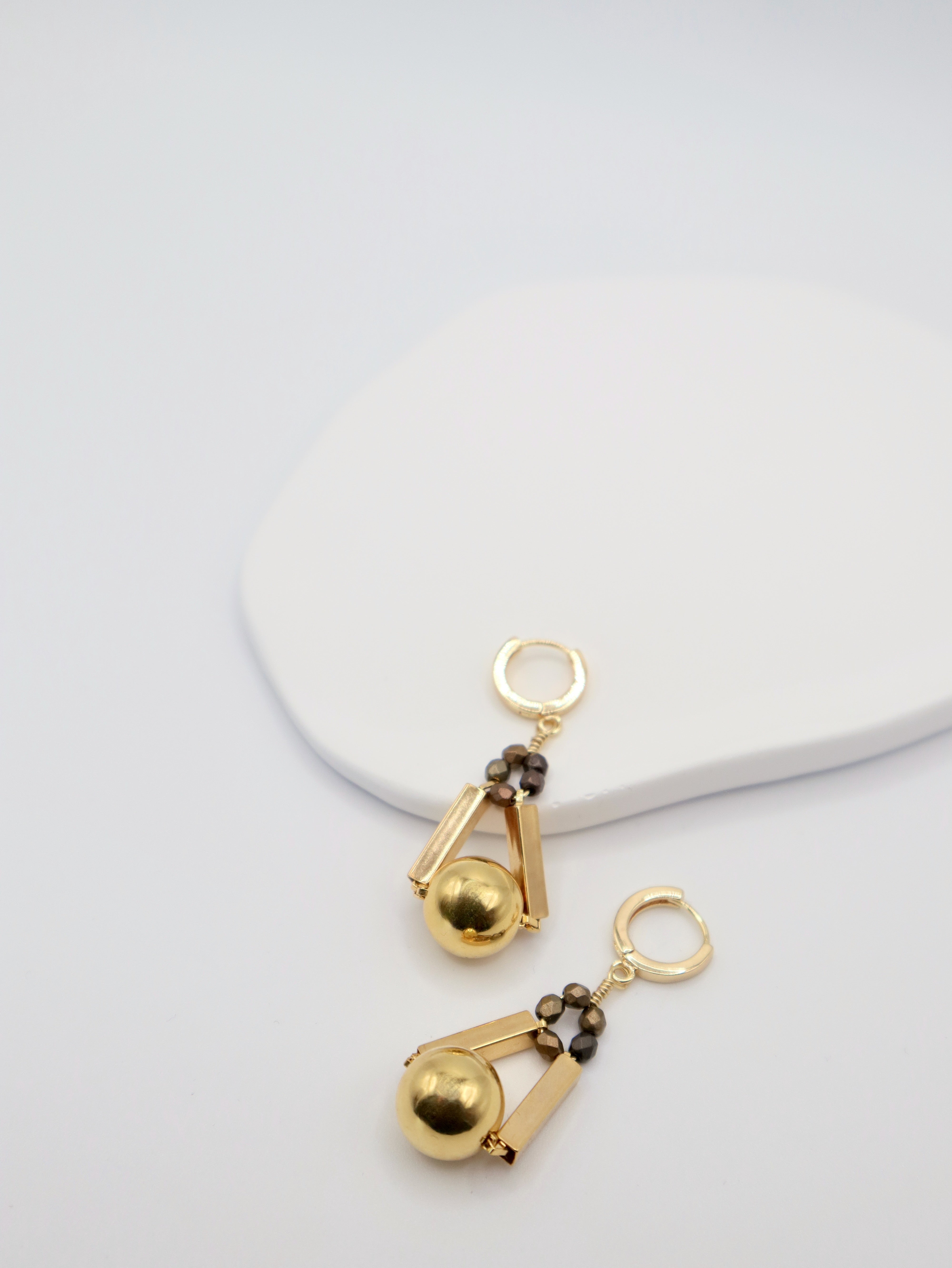 Gold earrings with bronze beads on a light gray background