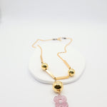 Gold necklace with a pink flower pendant on a white background
