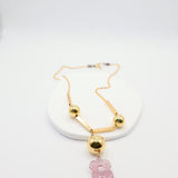 Gold necklace with a pink flower pendant on a white background