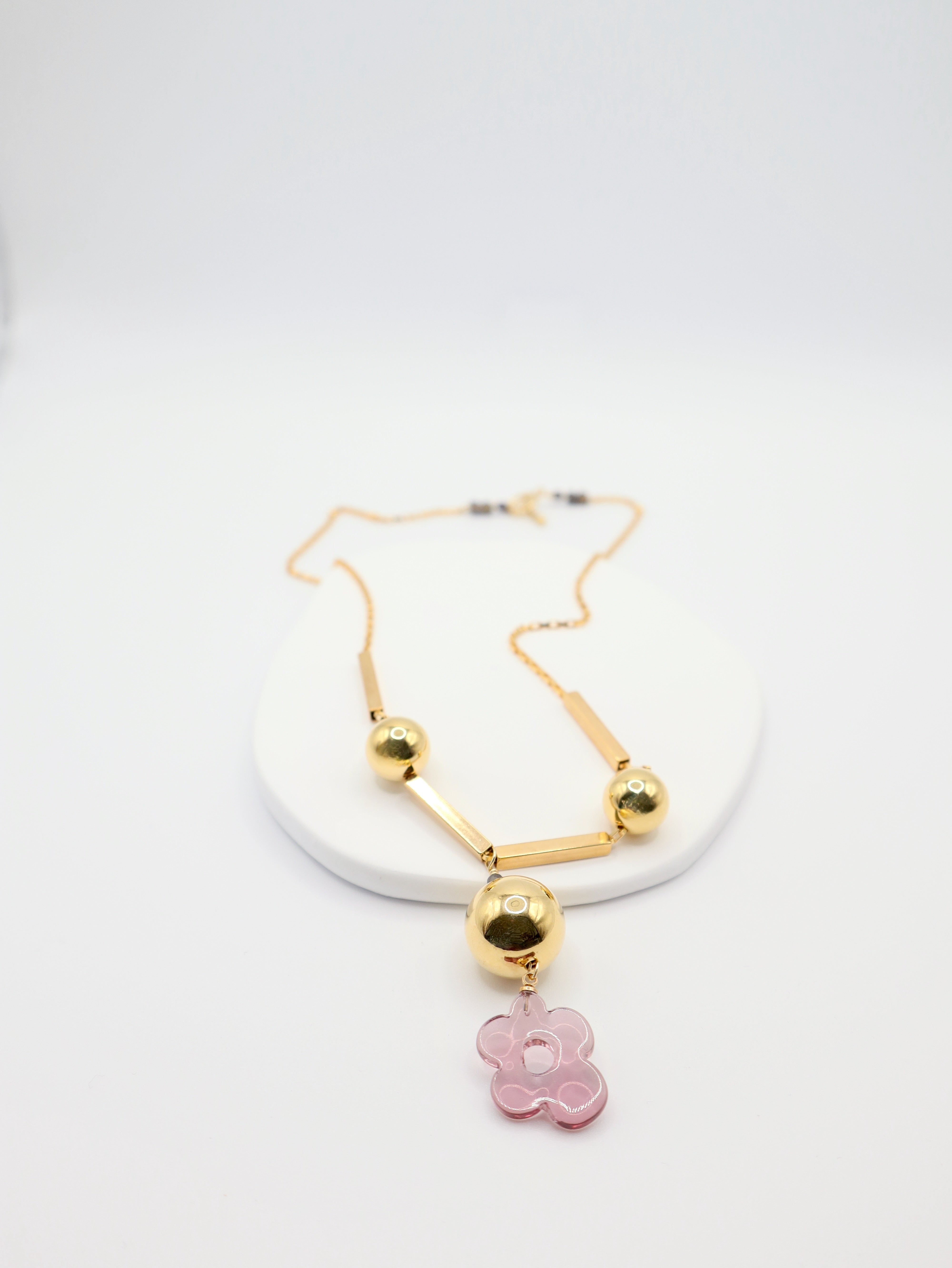 Gold necklace with a pink flower pendant on a white background