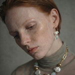 Woman wearing a necklace with gold , freshwater pearl and aquamarine beads with gold chain against a neutral background