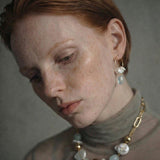 Woman wearing a necklace with gold , freshwater pearl and aquamarine beads with gold chain against a neutral background