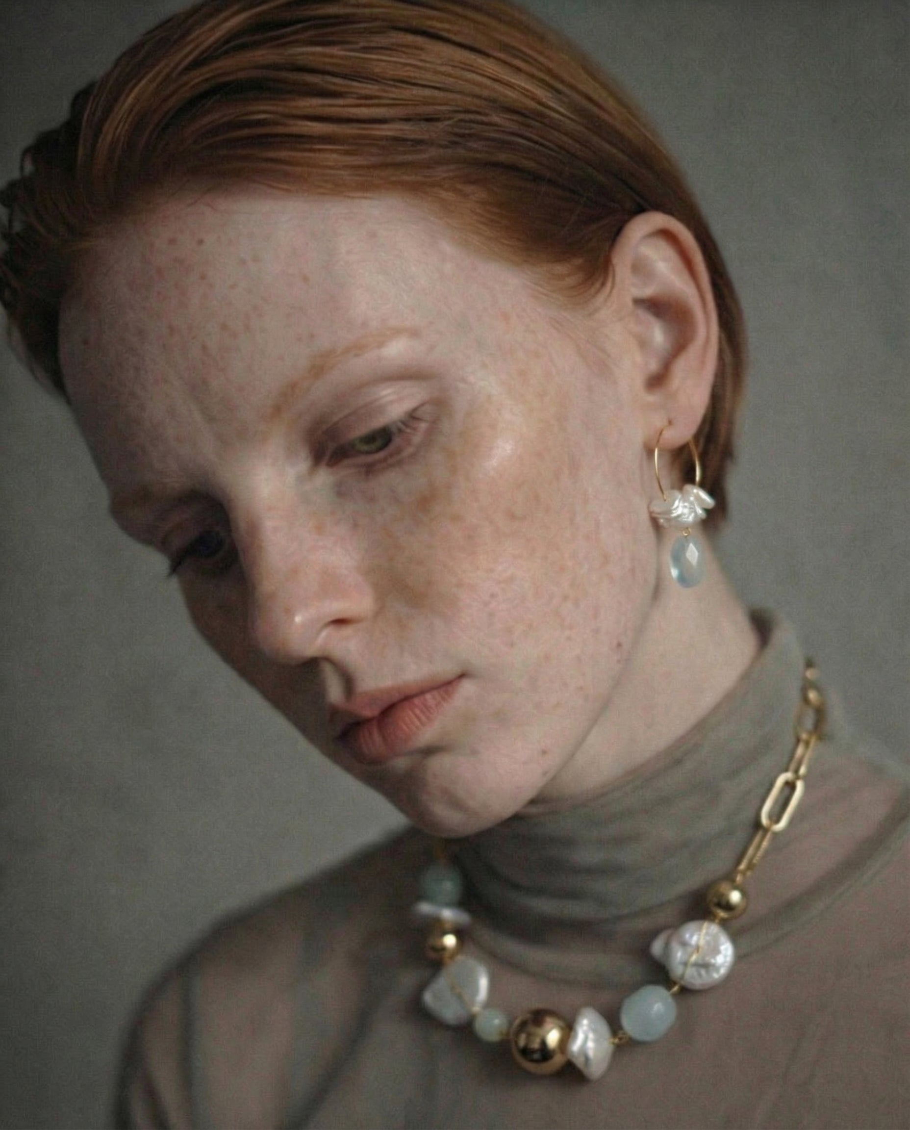 Woman wearing a necklace with gold , freshwater pearl and aquamarine beads with gold chain against a neutral background