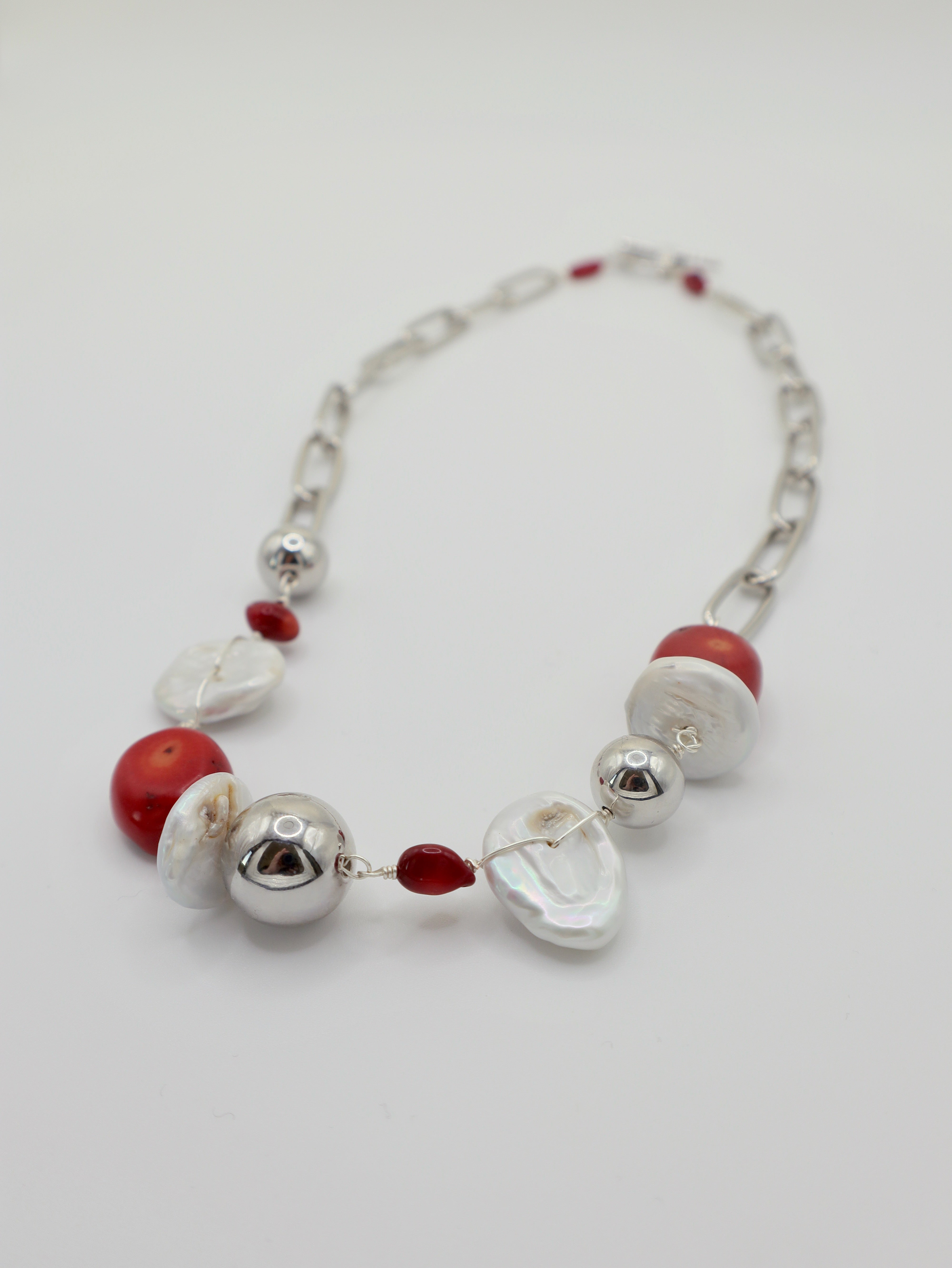 Necklace with red coral, freshwater pearls and silver beads on a white background