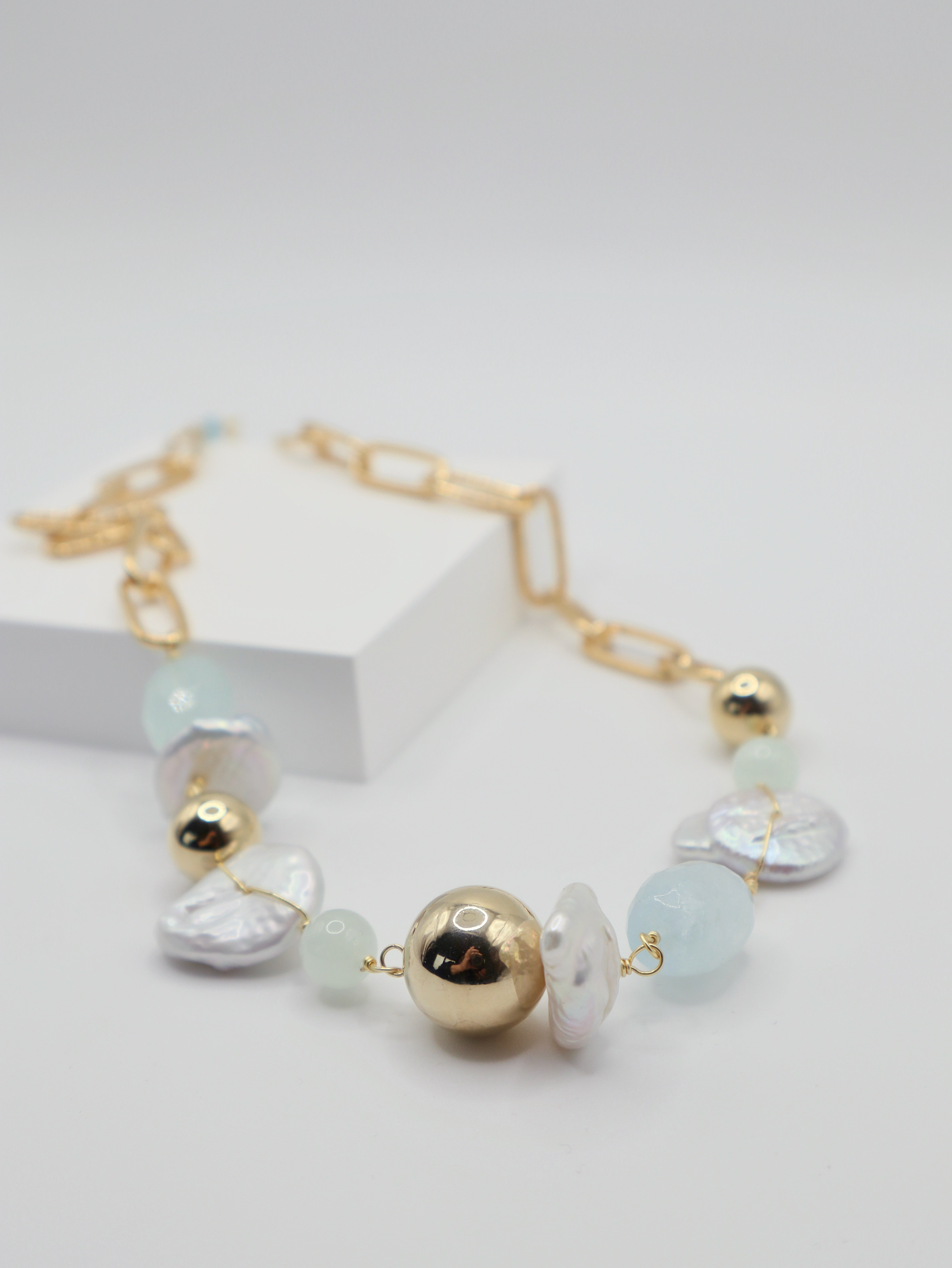 Necklace with gold spheres, freshwater pearls and aquamarine beads on a white background