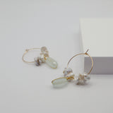 Gold hoop earrings with pearls and aquamarine stones on a light gray background