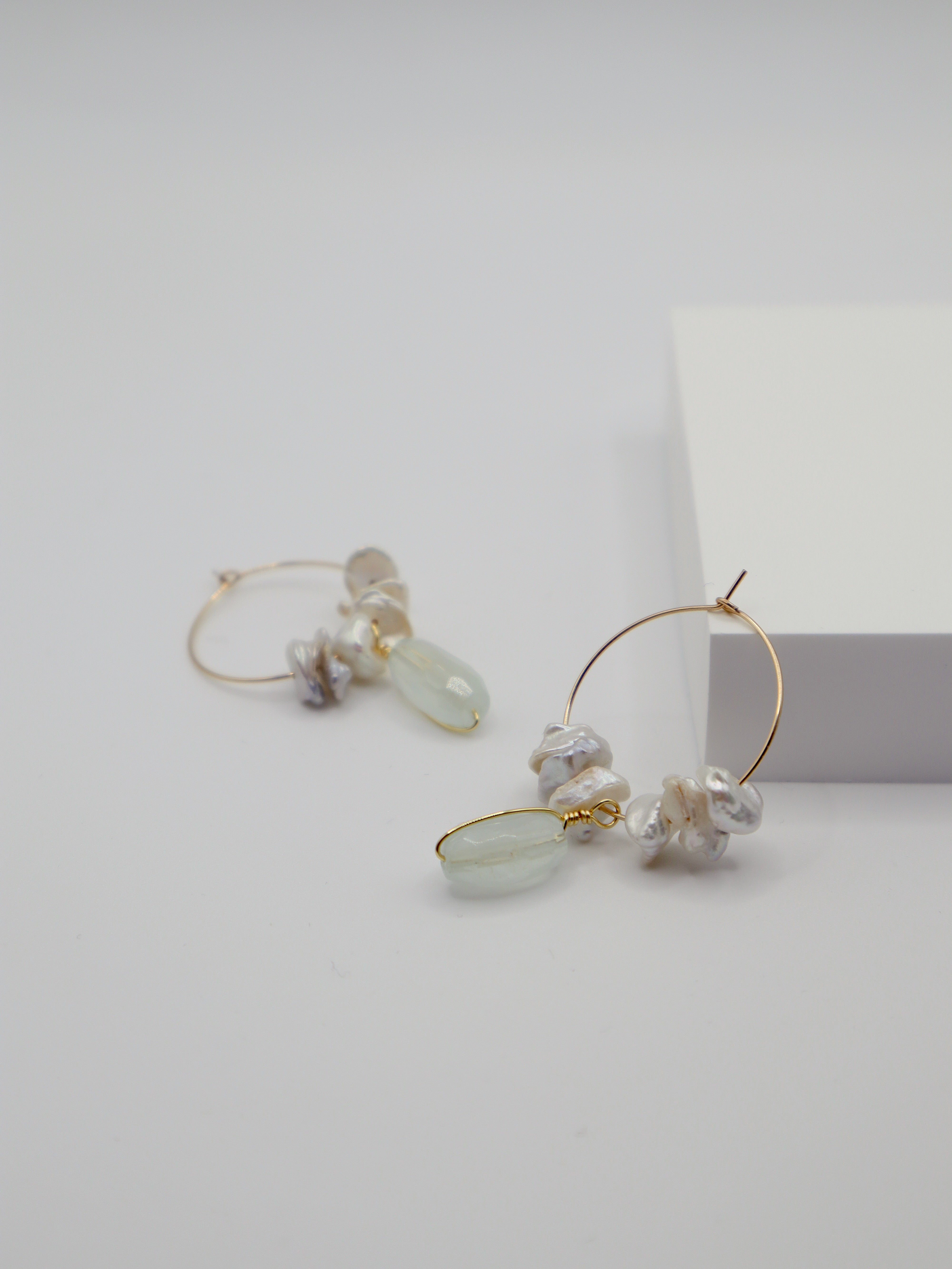 Gold hoop earrings with pearls and aquamarine stones on a light gray background