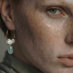 Close-up of a woman wearing gold hoop earrings with pearls and an aquamarine stone.