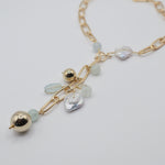 Gold necklace with freshwater pearl coins  and gold sphere beads on a light grey background