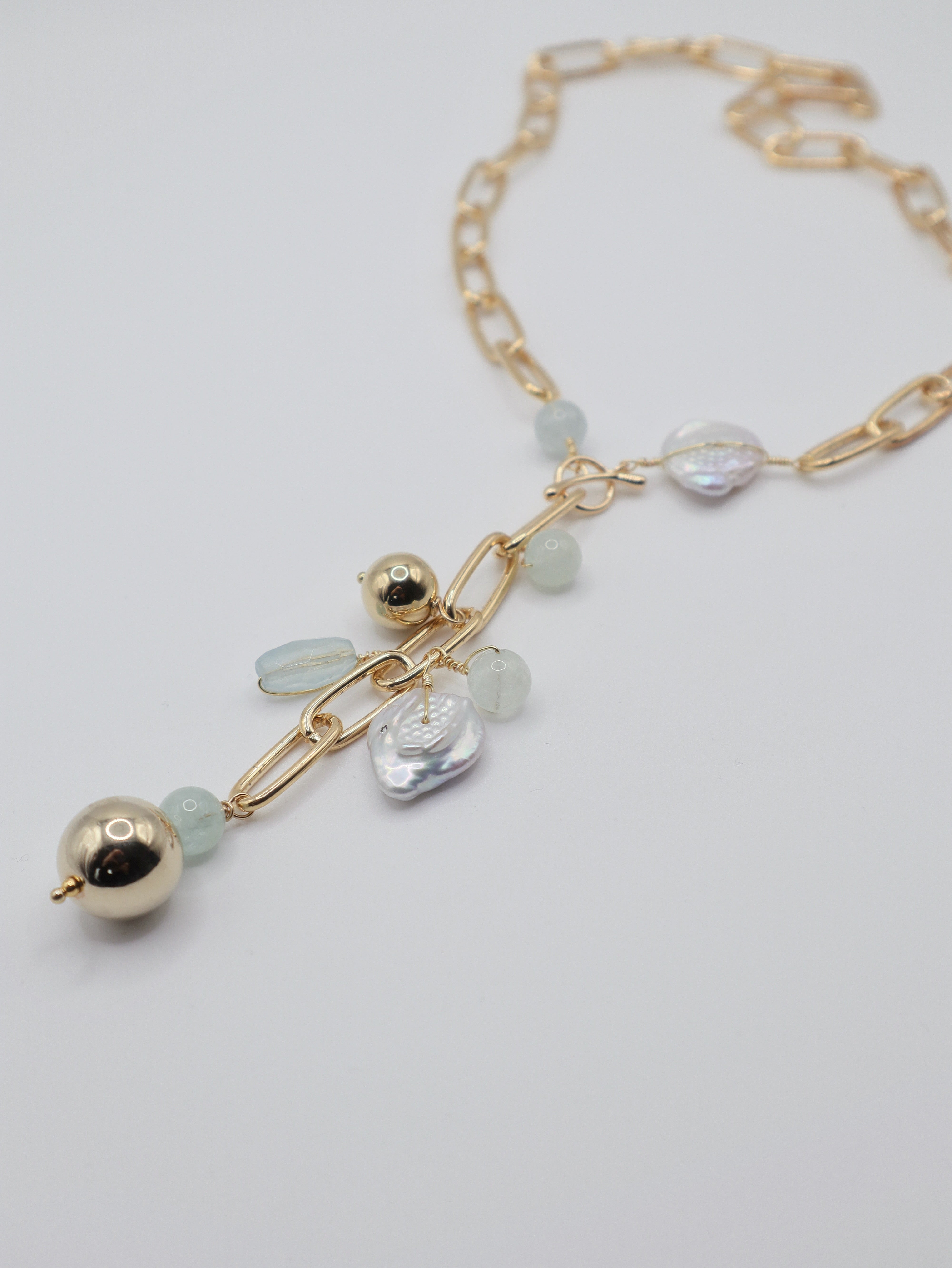 Gold necklace with freshwater pearl coins  and gold sphere beads on a light grey background