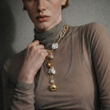 Woman wearing a gold necklace with spherical pendants and freshwater pearls against a neutral background