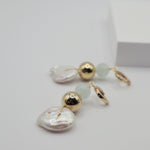 Pair of earrings with pearl coins, gold spheres and aquamarine beads on a light grey background