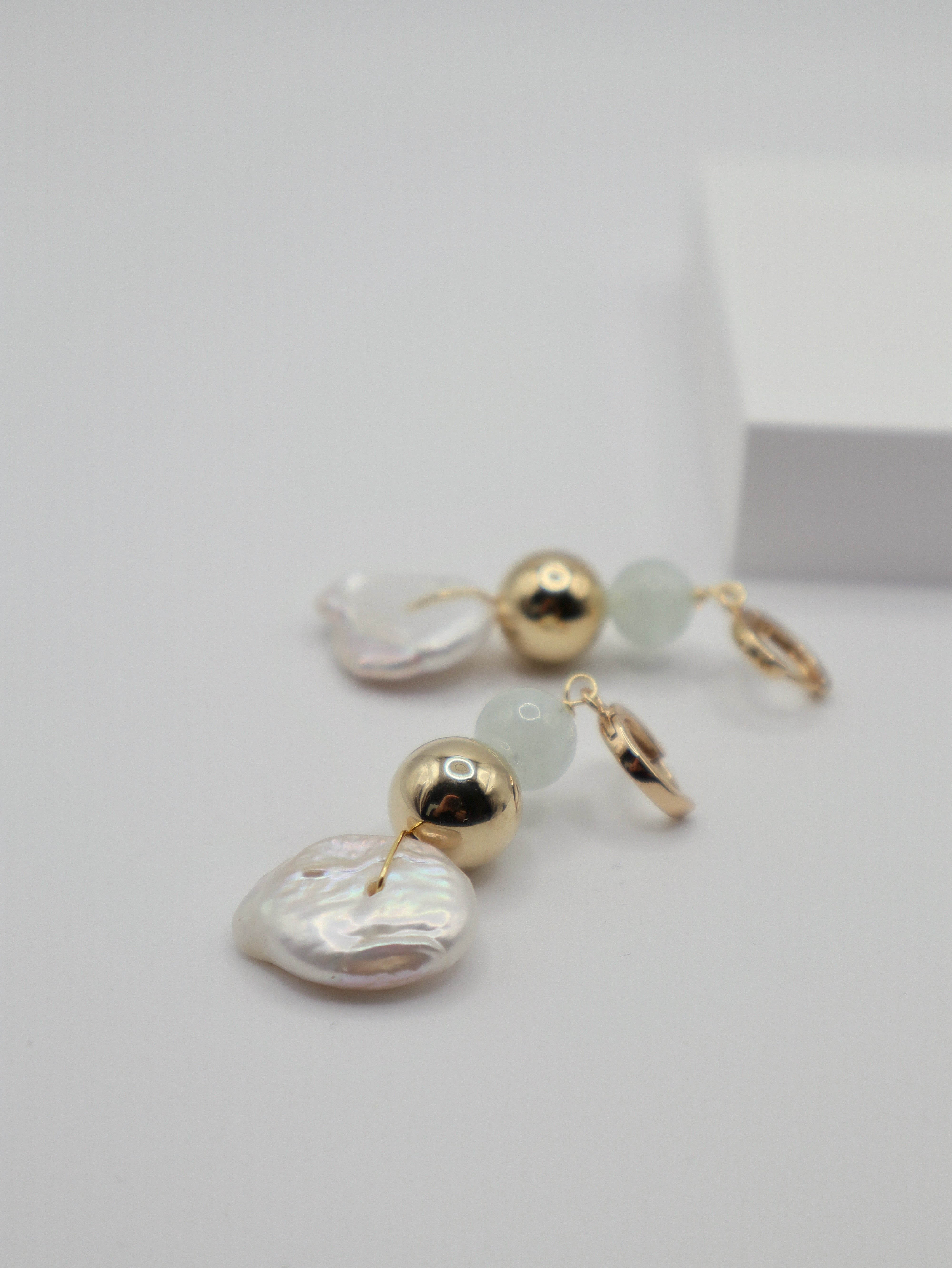 Pair of earrings with pearl coins, gold spheres and aquamarine beads on a light grey background