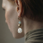 Close-up of an earring with pearls and gold elements on a neutral background