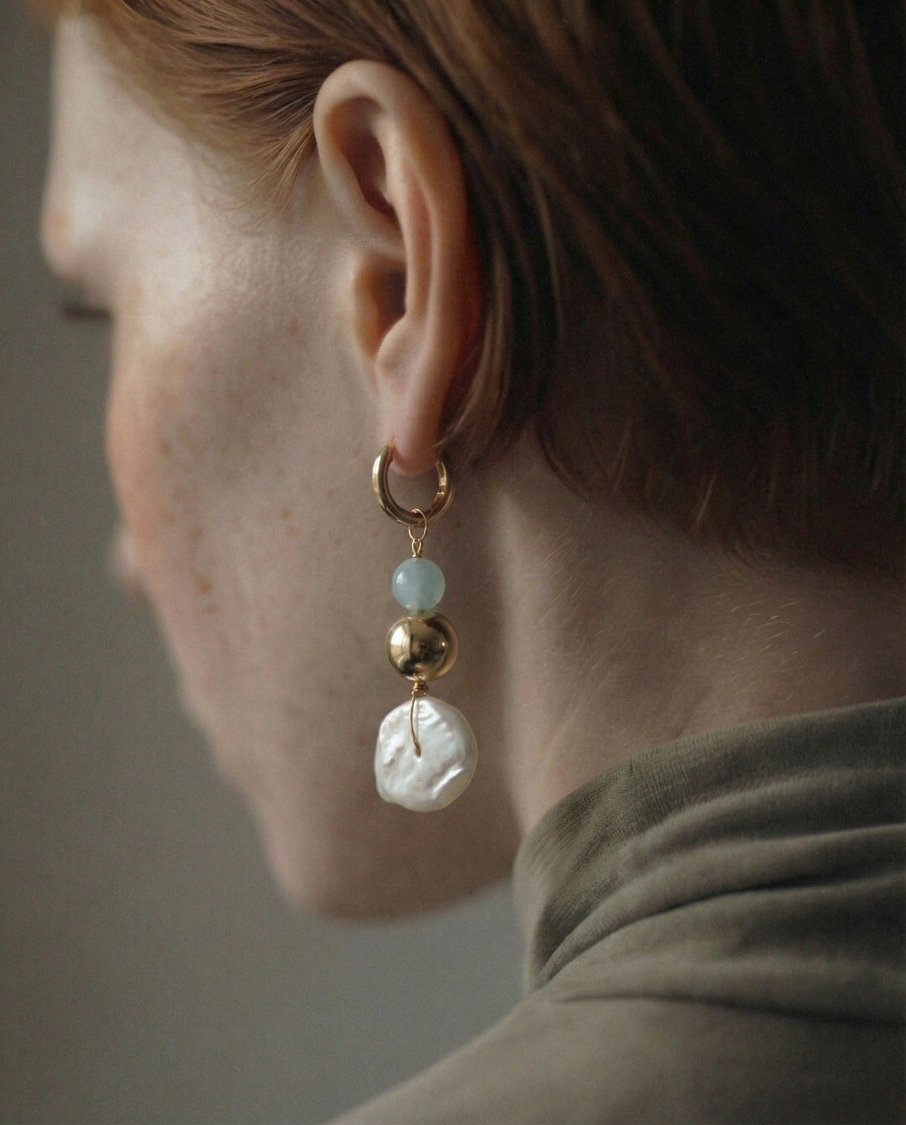 Close-up of an earring with pearls and gold elements on a neutral background