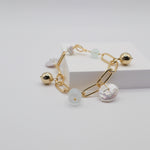 Gold link charm bracelet with freshwater pearls and aquamarine stones on a light grey background