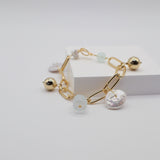 Gold link charm bracelet with freshwater pearls and aquamarine stones on a light grey background