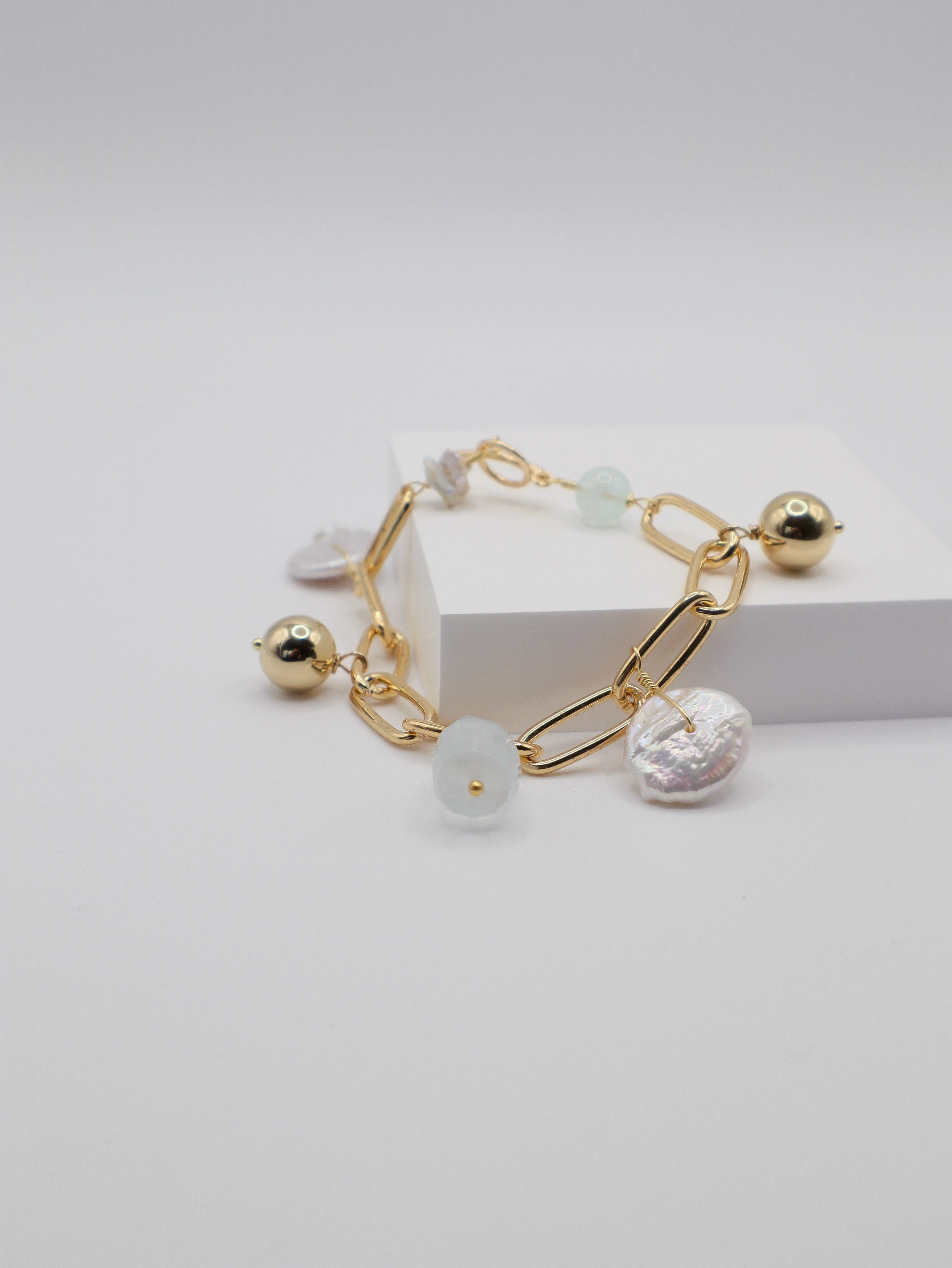 Gold link charm bracelet with freshwater pearls and aquamarine stones on a light grey background