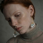 Close-up of a woman wearing oval link earrings with freshwater pearls against a neutral background