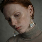 Close-up of a woman wearing oval link earrings with freshwater pearls against a neutral background