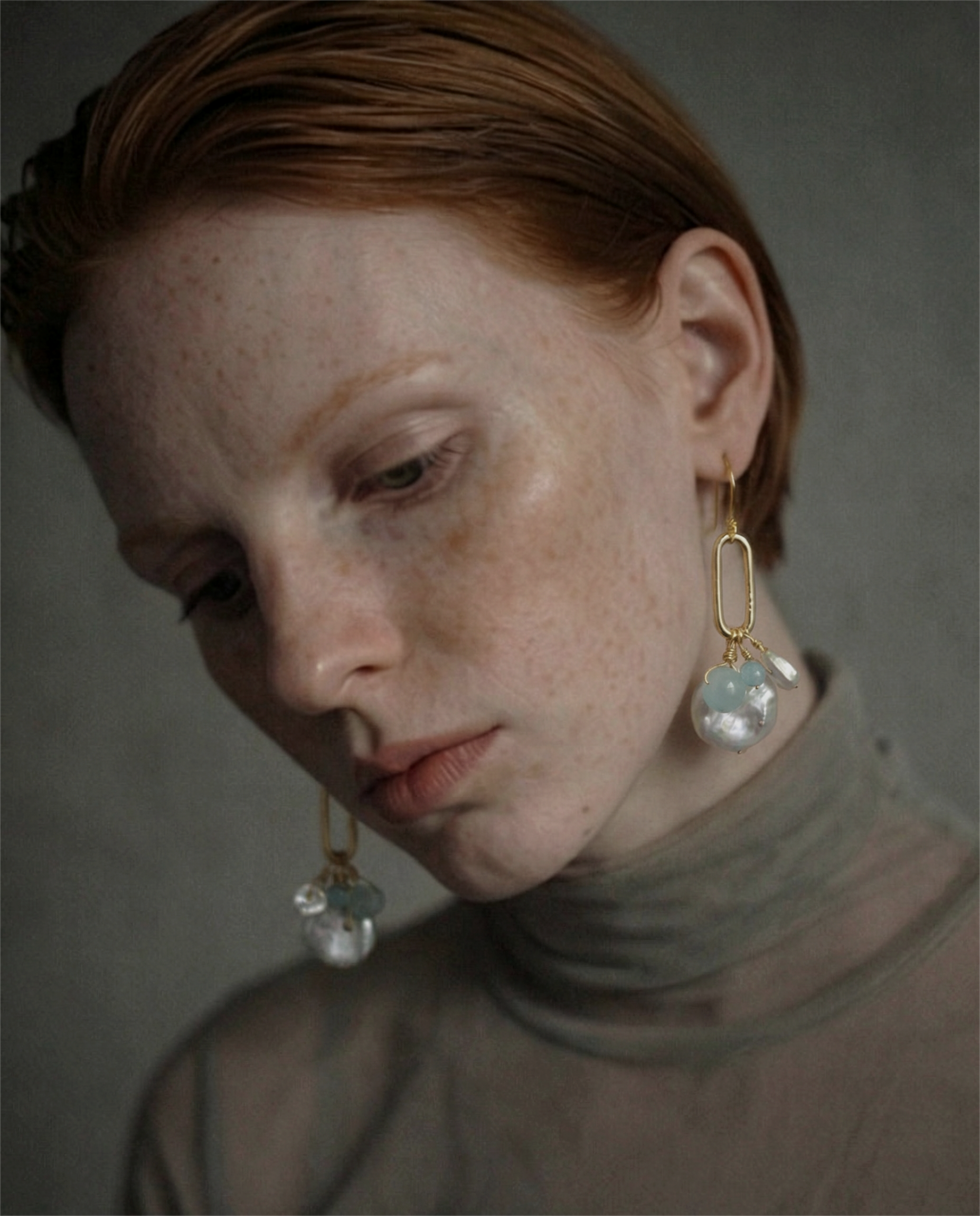 Close-up of a woman wearing oval link earrings with freshwater pearls against a neutral background
