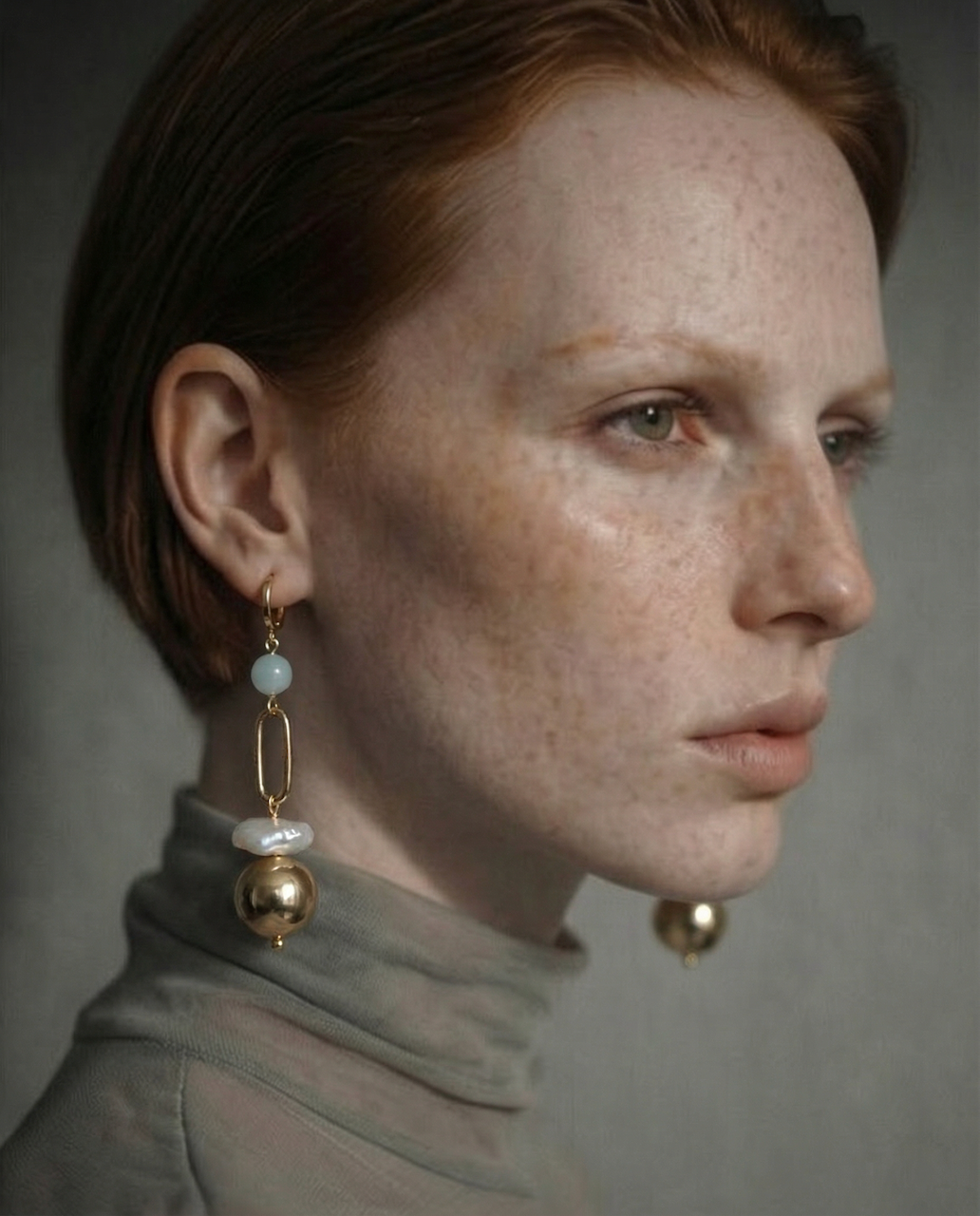 Close-up of a woman wearing gold , pearl and aquamarine earrings with a neutral background