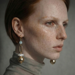 Close-up of a woman wearing gold , pearl and aquamarine earrings with a neutral background