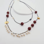 Two layered necklaces with burgundy shell pearls, black chain and gold accents on a white background