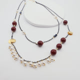 Two layered necklaces with burgundy shell pearls, black chain and gold accents on a white background