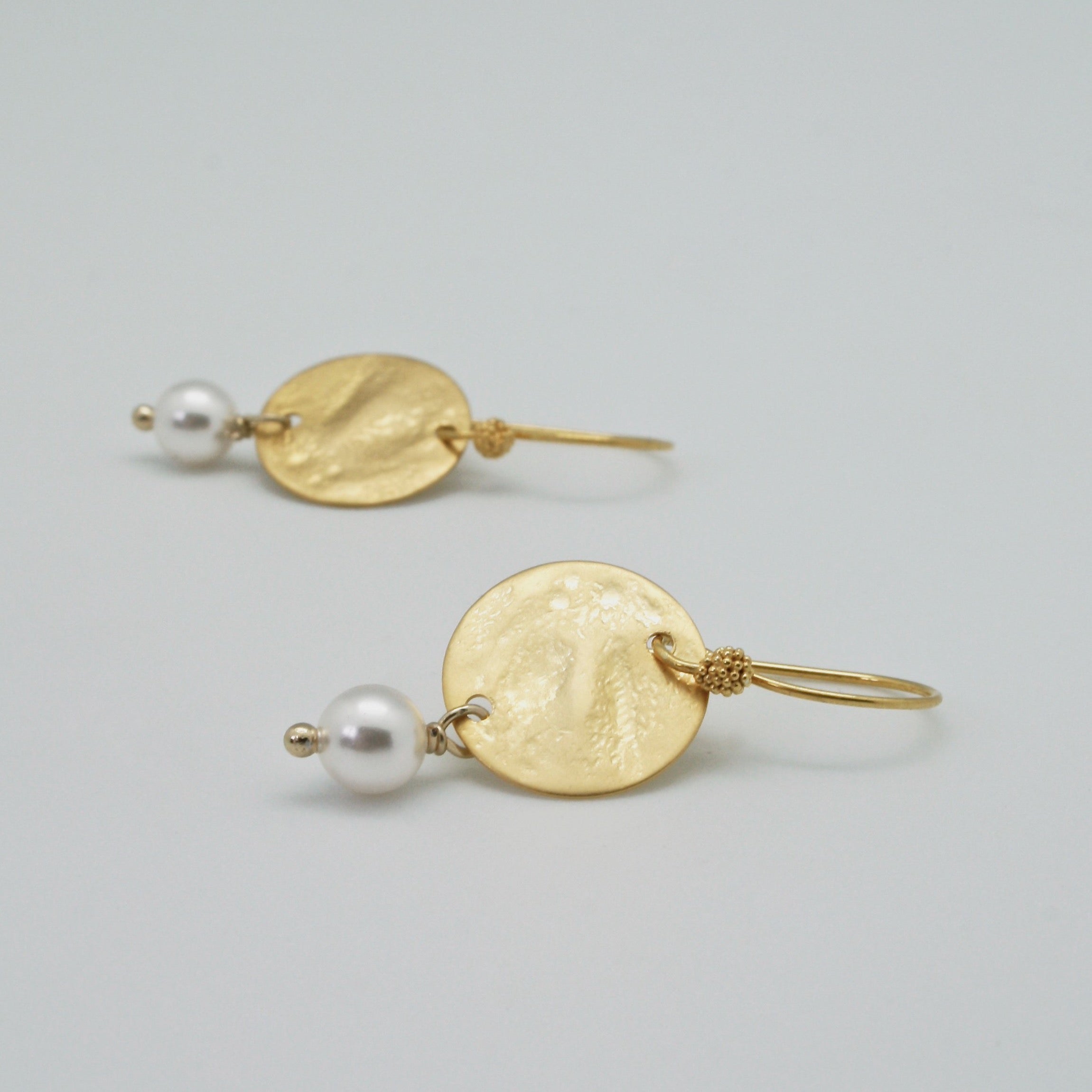 hammered gold disc earrings with white pearl drop lying flat by vivien walsh